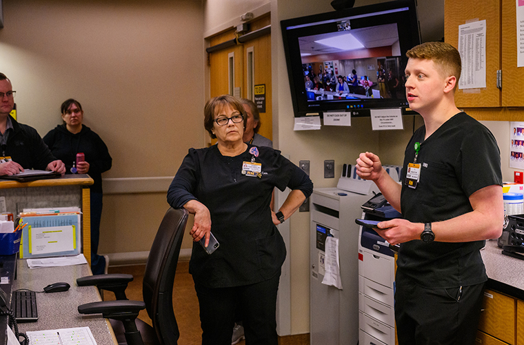TJ Headley, service line clinical supervisor, leads huddle as Sandy Harryman, nurse manager, looks on during the MICU huddle on the fifth floor. The MICU team on the third floor joined huddle remotely.